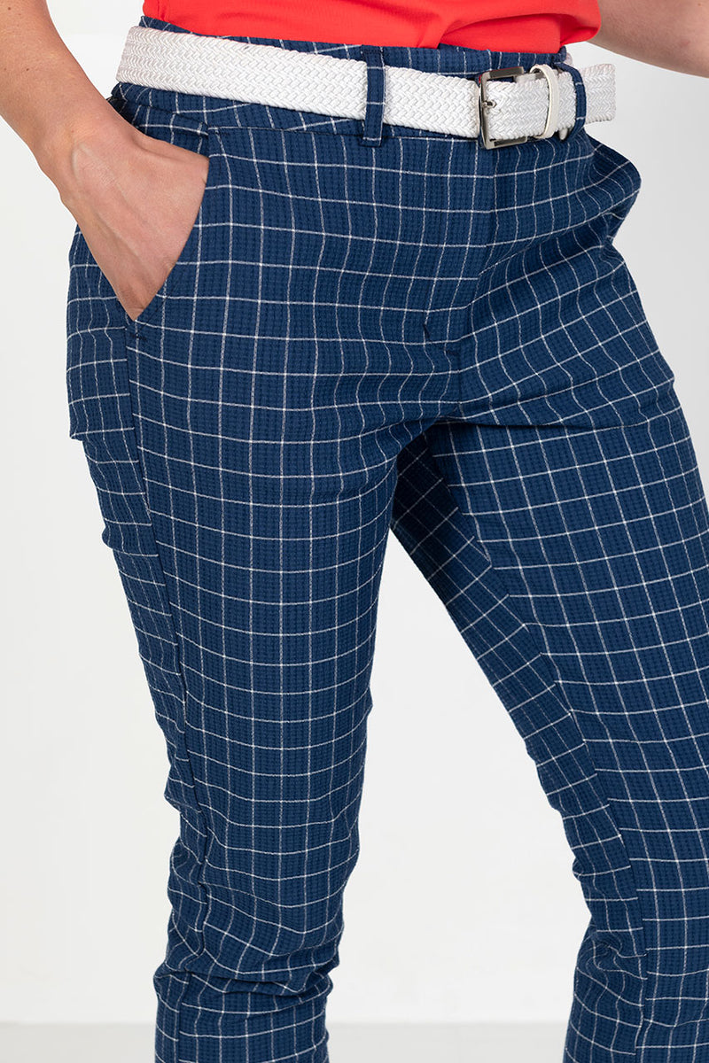 Woman wearing blue checkered golf pants with a white belt 