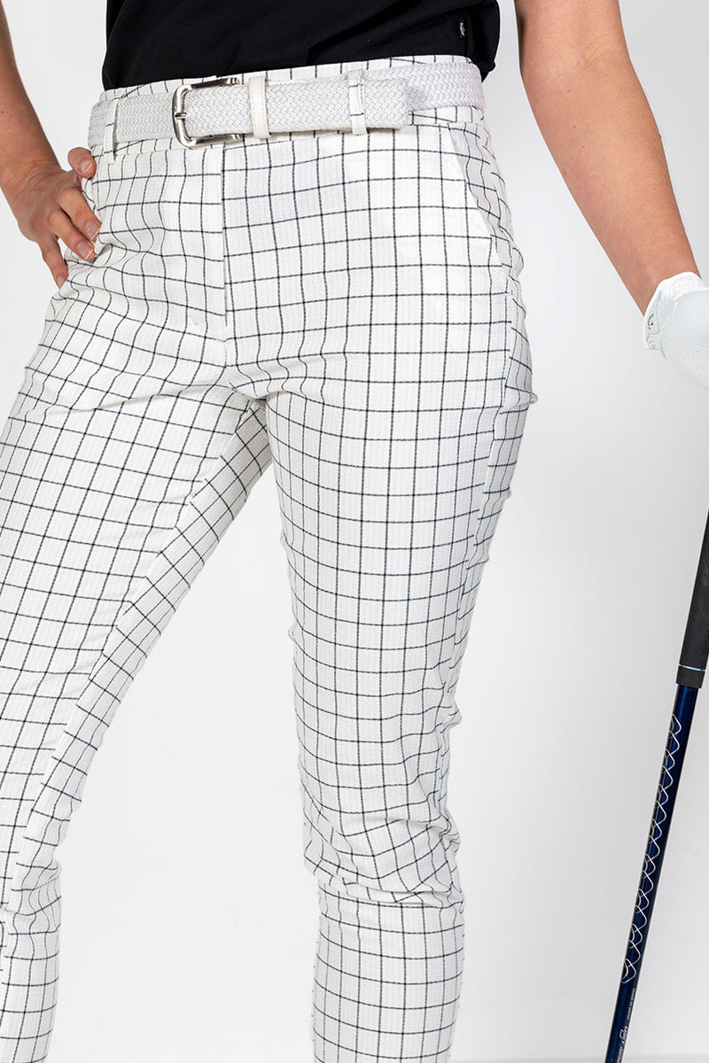 Woman in black sleeveless golf top and white and black checkered pants holding a golf club