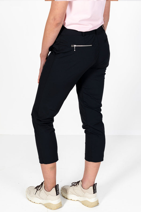 Woman wearing a pink golf polo shirt and lightweight black golf pants on a white background