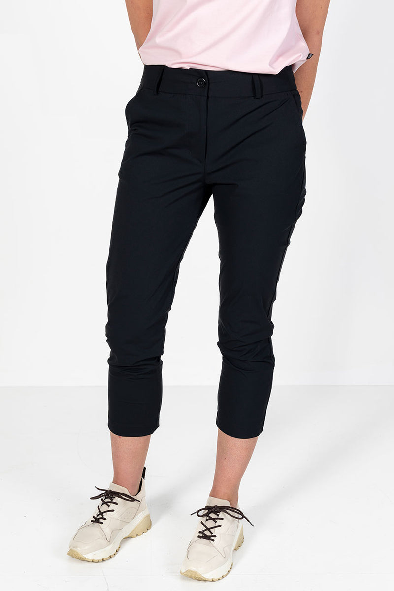 Woman wearing a pink golf polo shirt and lightweight black golf pants on a white background