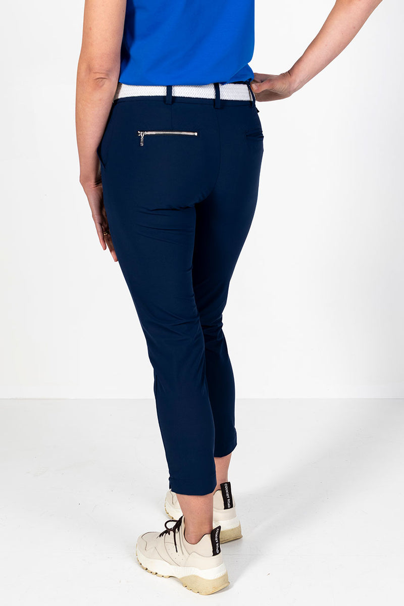 Woman wearing a cobalt cap sleeve golf polo shirt and lightweight navy golf pants on a white background