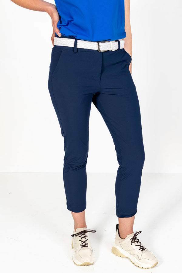 Woman wearing a cobalt cap sleeve golf polo shirt and lightweight navy golf pants on a white background