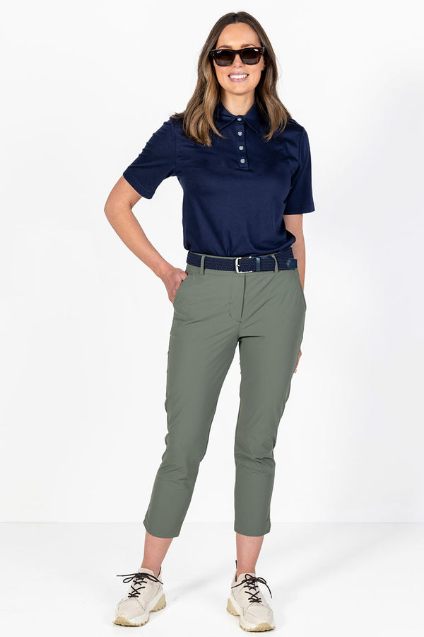 Woman wearing a navy golf polo shirt and olive lightweight golf pants on a white background